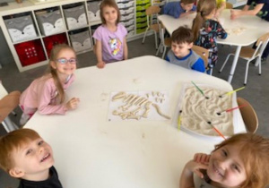 dzieci układają w całość odkryte w piasku elementy szkieletu dinozaura